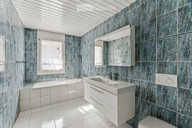 Modern bathroom with blue marble tiles, white fixtures, a bathtub, a sink with a cabinet, and a large mirror.