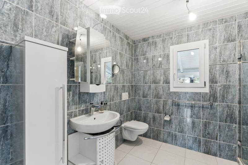 Modern bathroom with grey marble tiles, white sink, toilet, and mirrored cabinet.