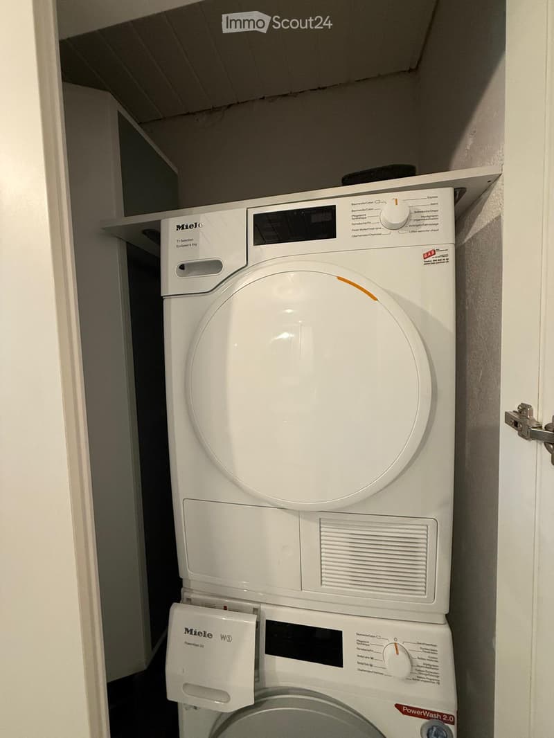 A compact bathroom with a stacked Miele washing machine and dryer unit, featuring control panels and dials.