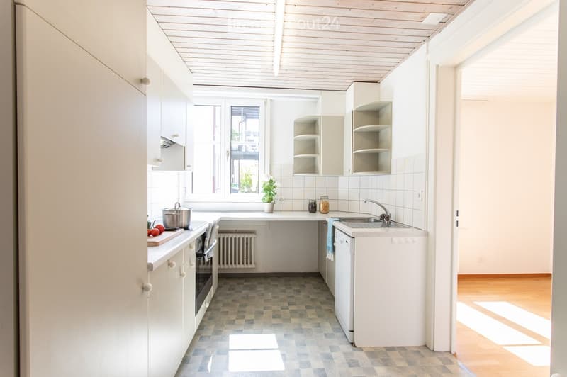 Bright kitchen with white cabinets, a checkered floor, and a window overlooking a view. Includes a sink, oven, dishwasher, and a small plant on the counter.