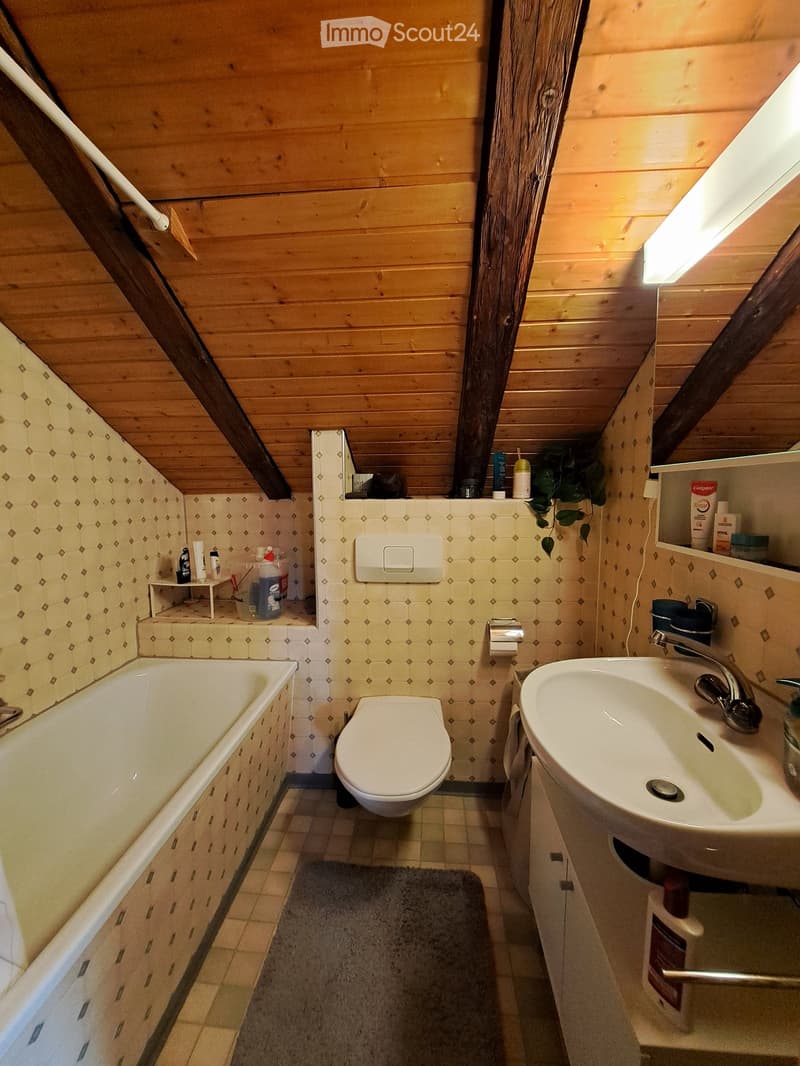 Cozy attic bathroom with wooden walls and ceiling, featuring a bathtub, toilet, sink, and small shelf with toiletries.
