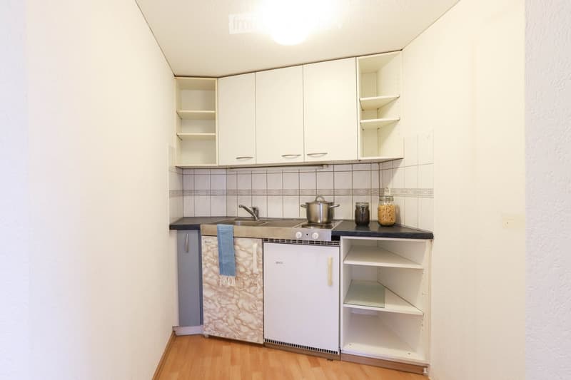 Compact kitchen with white cabinets, a sink, stove, and refrigerator. Wooden flooring and tiled backsplash.