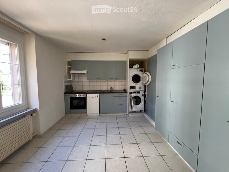 Modern kitchen with grey cabinets, tiled floor, oven, dishwasher, sink, and a washing machine in a separate area.