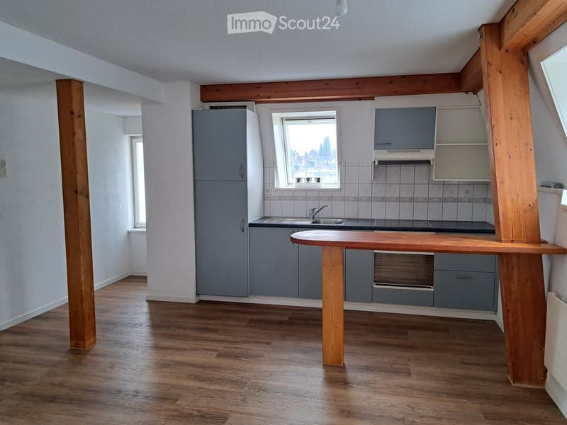 Modern kitchen with wooden flooring, grey cabinets, a central island table, and a window overlooking a view.
