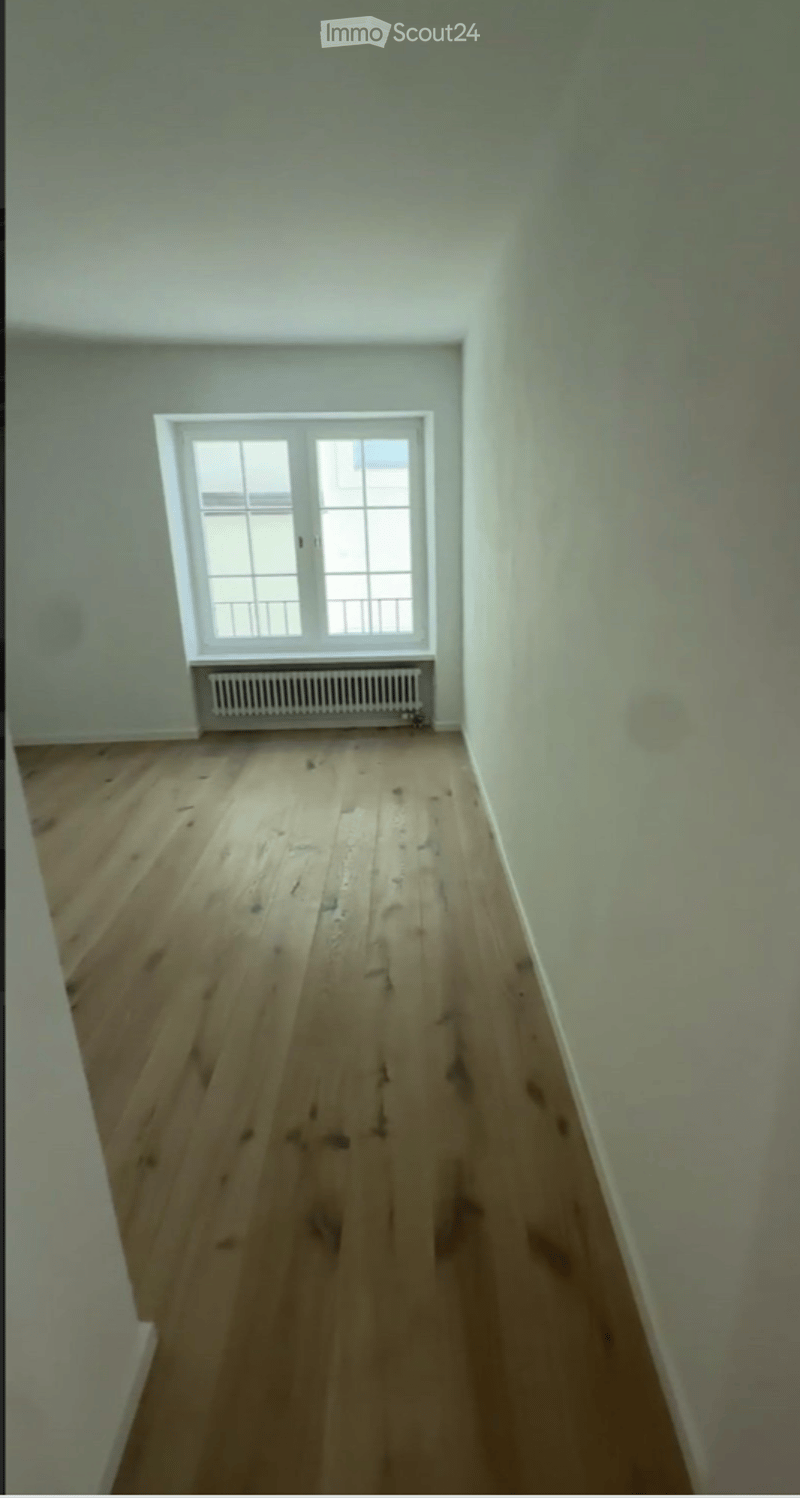 Empty room with wooden flooring, white walls, and a single window with white frame and multiple panes. A radiator is placed below the window.
