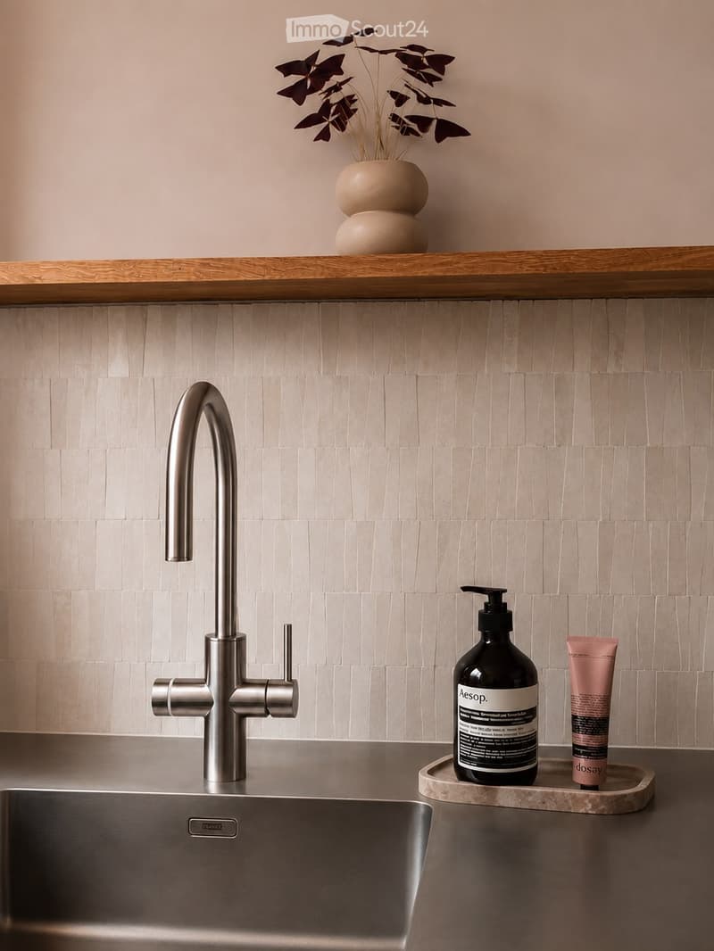 Modern bathroom sink area with a sleek chrome faucet, stainless steel sink, and decorative items including a vase with dried flowers and toiletries on a wooden shelf.