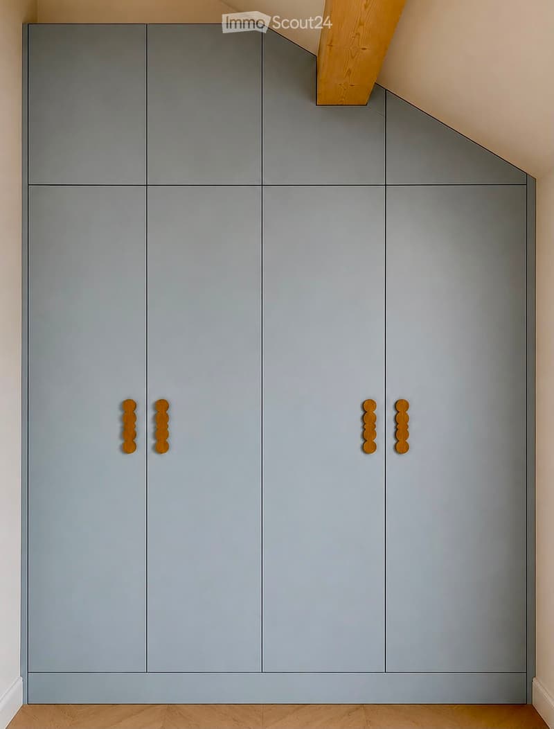 Modern grey built-in wardrobe with wooden handles in a room with light wooden flooring and white walls.
