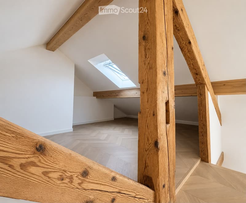 An empty attic space with wooden beams, a skylight window, and wooden flooring.
