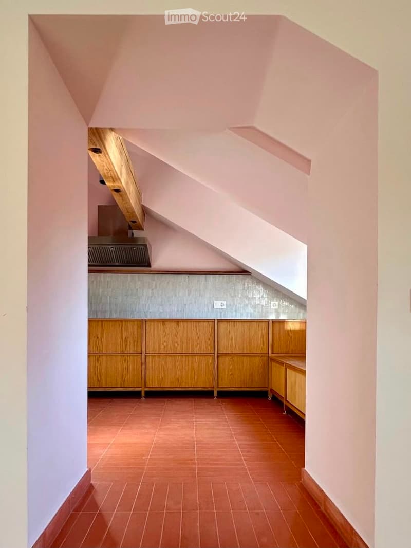 Modern kitchen with wooden cabinets, tiled floor, and a range hood, featuring a slanted ceiling and ample natural light.