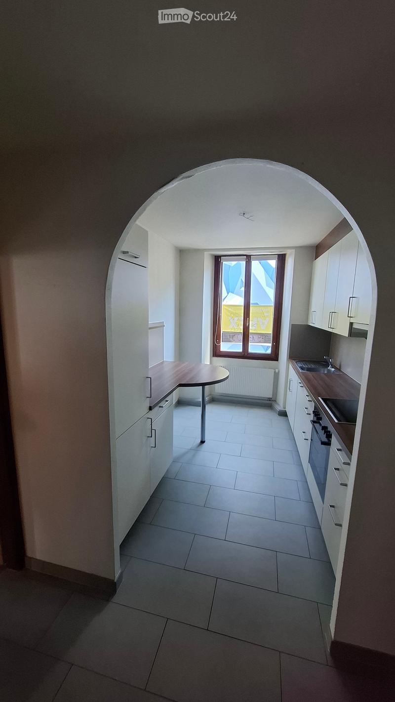 Modern kitchen with white tiled floor, white cabinets, a wooden countertop, a sink, and an oven. A small round table is placed near the window.