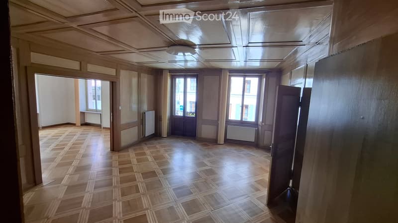 Empty room with wooden tiled floor, large windows, and decorative ceiling. No furniture or equipment present.