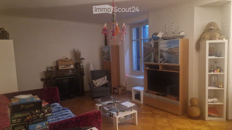 Living room with a red sofa, armchair, coffee table, fireplace, chandelier, shelves with decorative items, and a view of a canal through the window.