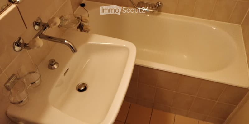 Bathroom with a white sink, chrome faucet, and bathtub. Beige tiles on walls and floor.