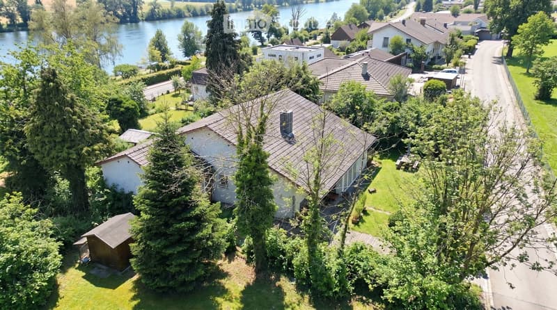 Aerial view of a residential area with multiple houses, surrounded by trees and a lake in the background.