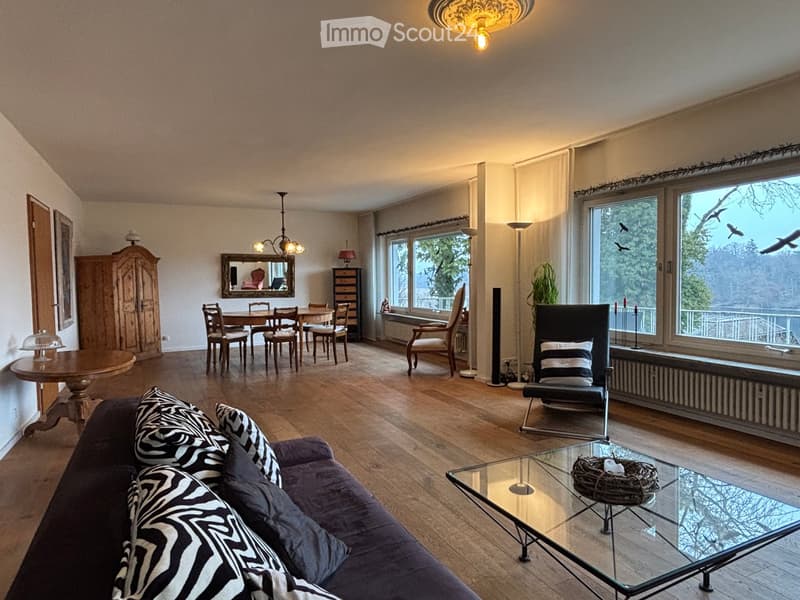 large living room with wooden floor, large windows, dining table, chairs, couch with zebra print pillows, glass table, mirror, chandelier, wooden cabinet, radiator