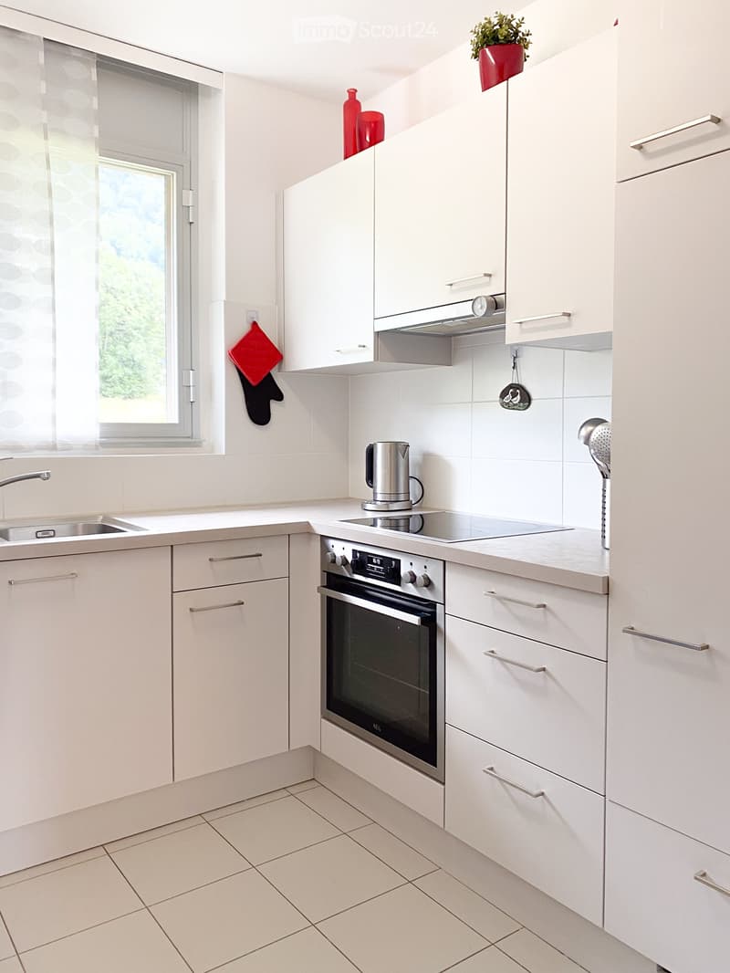 Modern kitchen with white cabinets, stainless steel appliances, and a large window with blinds.
