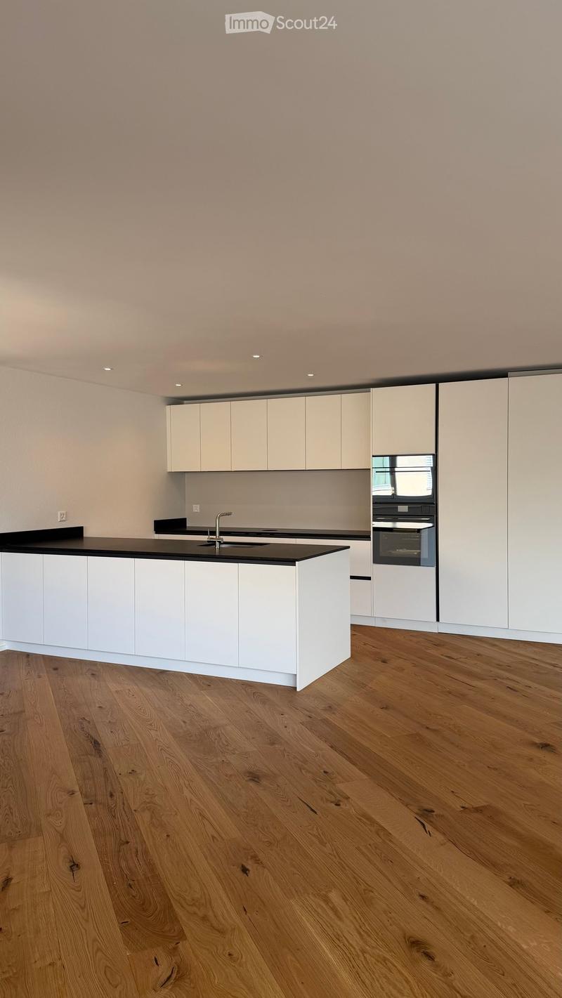 Modern kitchen with white cabinets, black countertop, and wooden flooring.