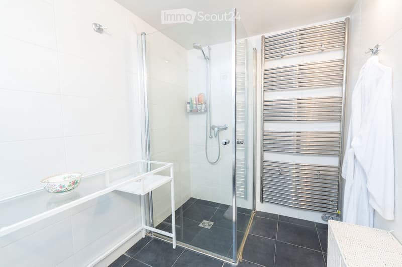 Modern bathroom with a bathtub, glass-enclosed shower, towel rack, and a small table with a decorative bowl.