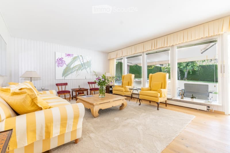 Bright living room with large windows, yellow armchairs, striped sofa, coffee table, side tables, and decorative vases.
