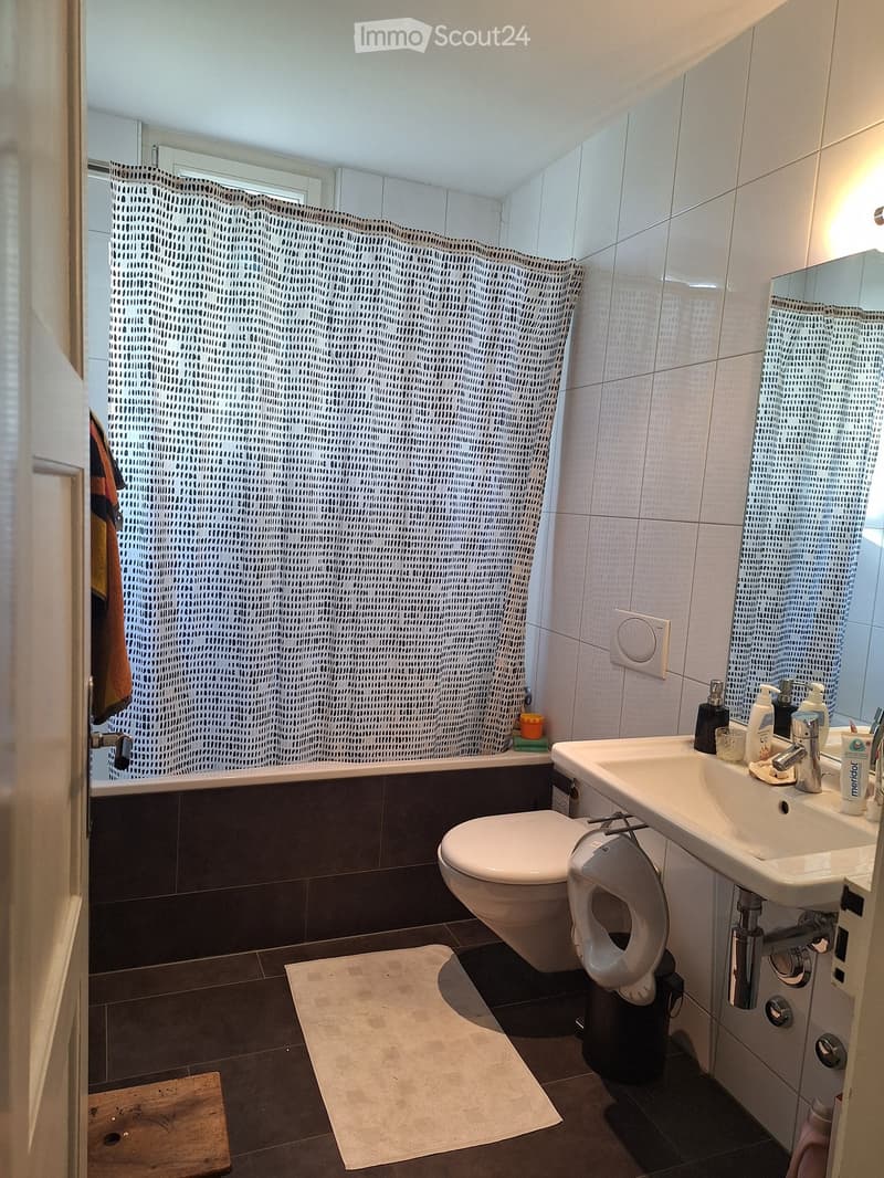 Modern bathroom with a toilet, sink, bathtub, and shower curtain. Includes a mirror, soap dispenser, and a towel on the floor.