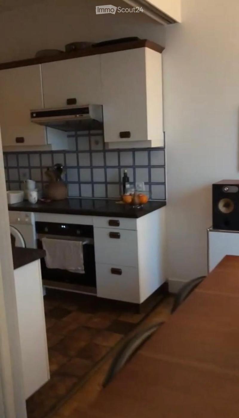 Modern kitchen with white cabinets, black countertop, built-in oven, and a small island. The backsplash features a blue and black tile design. A few kitchen items, including a bottle, bowl, and cup, are placed on the countertop.