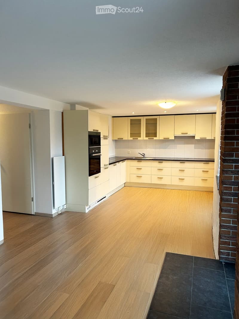 Empty kitchen with light-colored cabinets, a built-in oven, and wooden flooring.