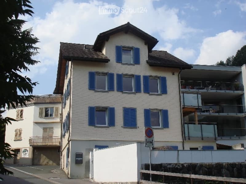Multi-story residential building with white facade, blue shutters, and balconies on the upper floors.