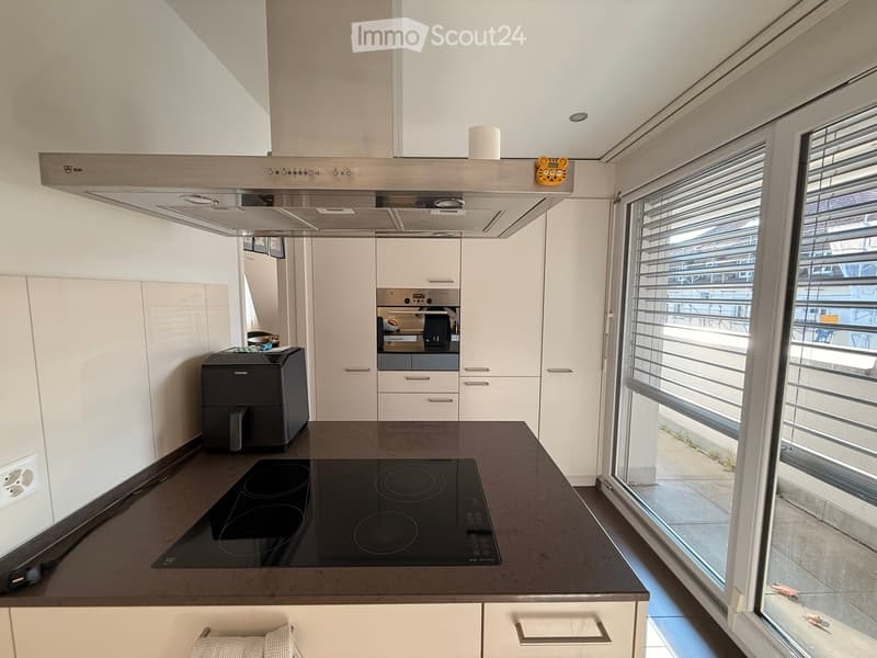 Modern kitchen with white cabinets, black countertop, induction stove, range hood, and a printer on the counter.