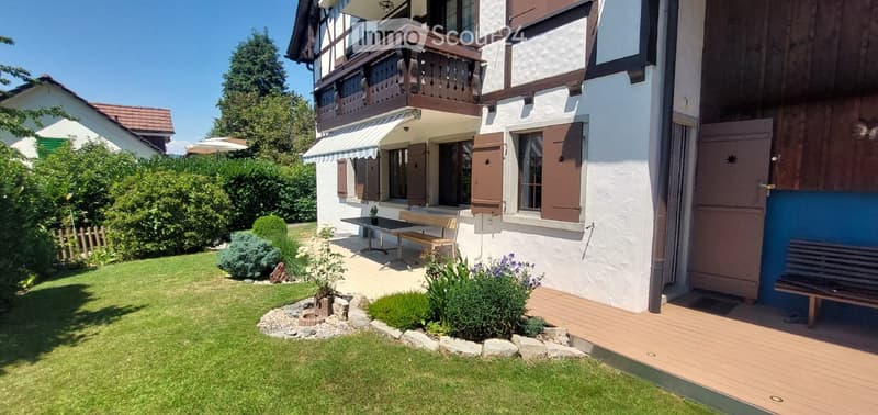 Well-maintained garden with a wooden deck, small seating area, and a balcony overlooking the yard.