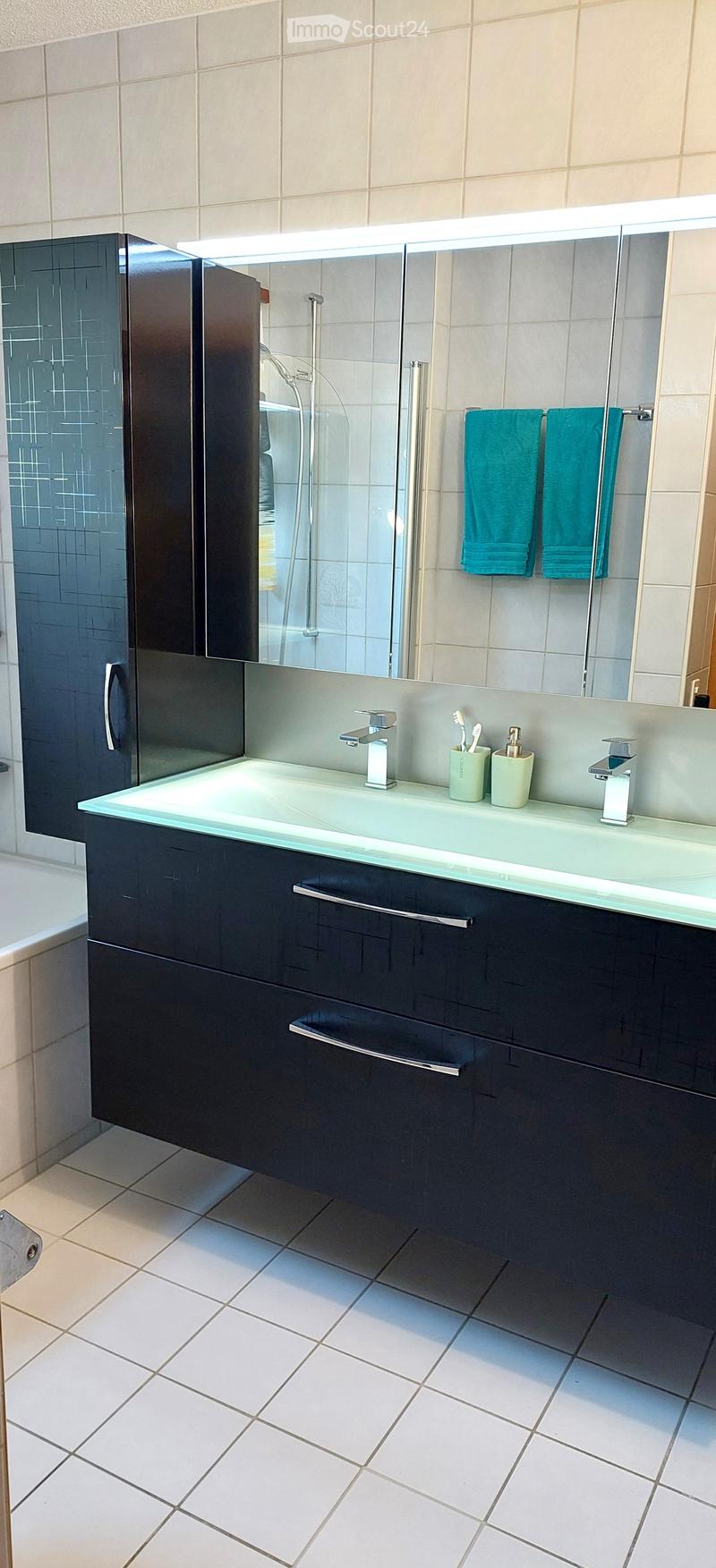 Modern bathroom with a large sink, sleek dark cabinets, a mirror with built-in lighting, and a glass-enclosed shower area.
