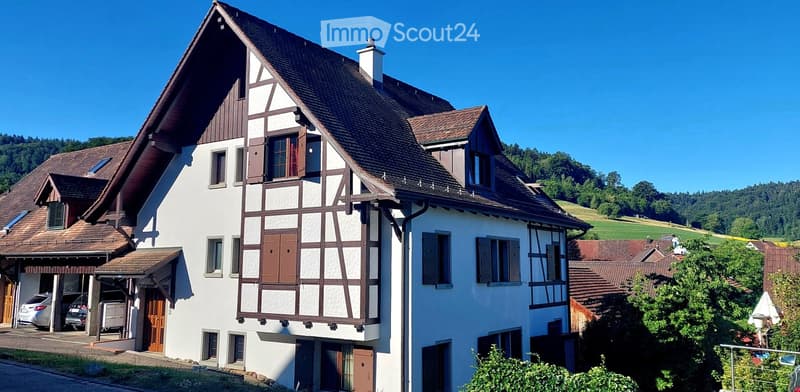 Two-story house with white walls, brown wooden trim, multiple windows, garage, and parking area.
