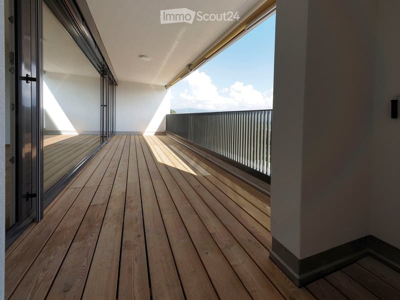Wooden deck with large windows, modern railing, and a view of the sky and distant landscape.