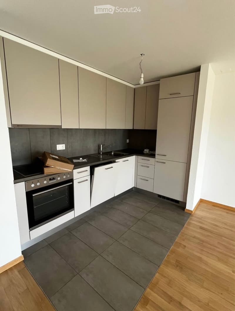 Modern kitchen with white cabinets, grey tiles, and a wooden floor. Features an oven, sink, and faucet.