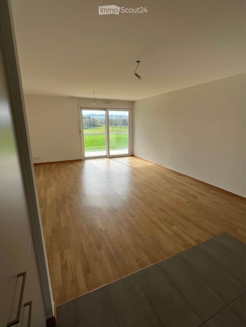 Empty room with wooden flooring, large sliding glass door leading to outdoor area, white walls, and recessed lighting.