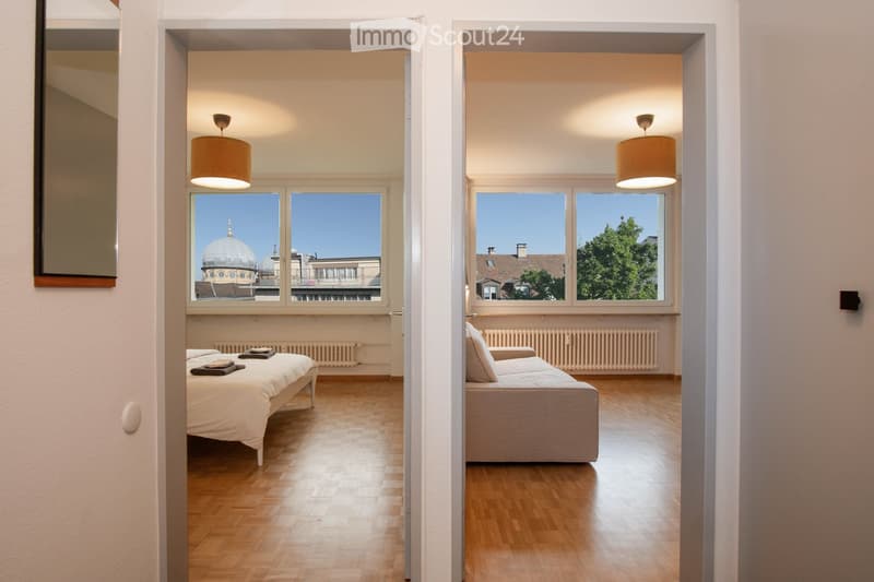 Bedroom with bed, couch, and large windows with city view