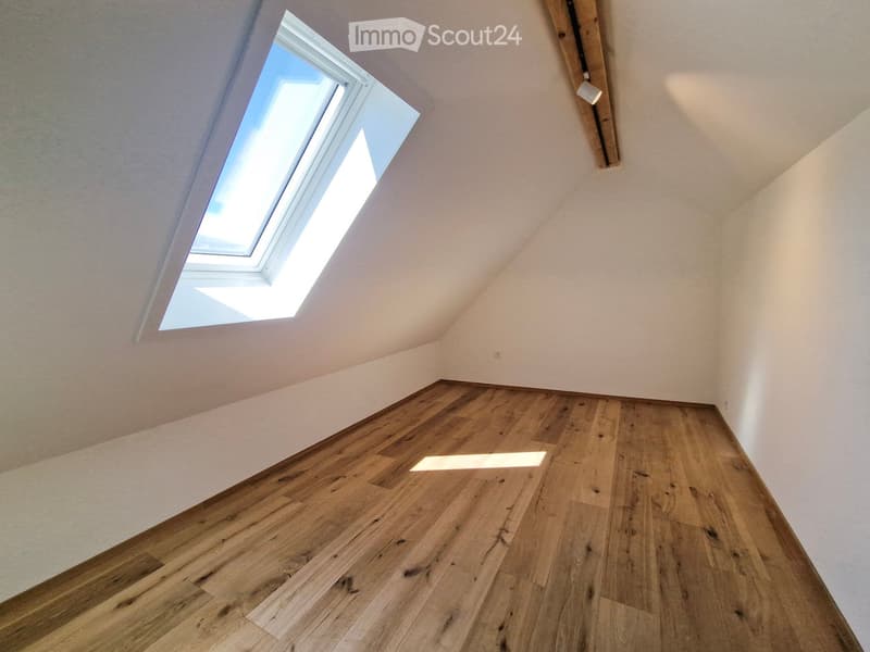 Empty attic space with wooden flooring and a skylight window, featuring white walls and a slanted ceiling.