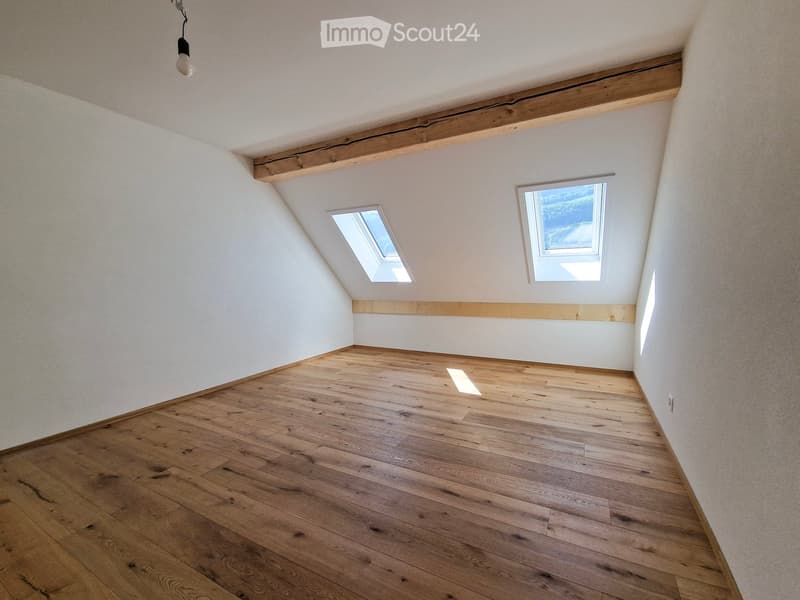 Empty attic room with wooden flooring, white walls, exposed wooden beams, and skylight windows.