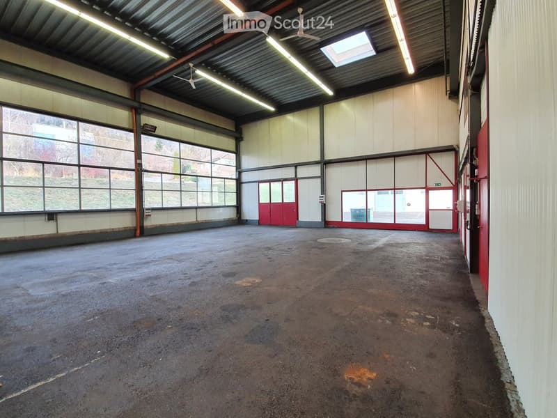 Large, empty industrial-style room with concrete floor, white walls, large windows, and red doors.
