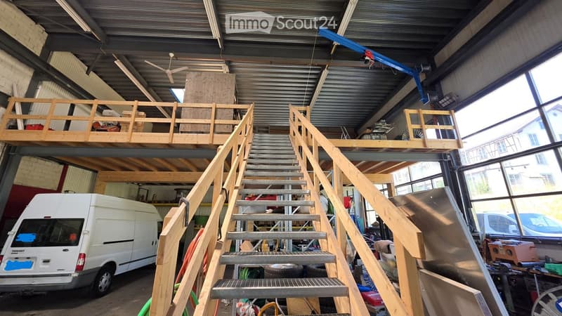 Large industrial-style garage with a metal roof, wooden staircase leading to an upper loft area, and a white van parked inside.