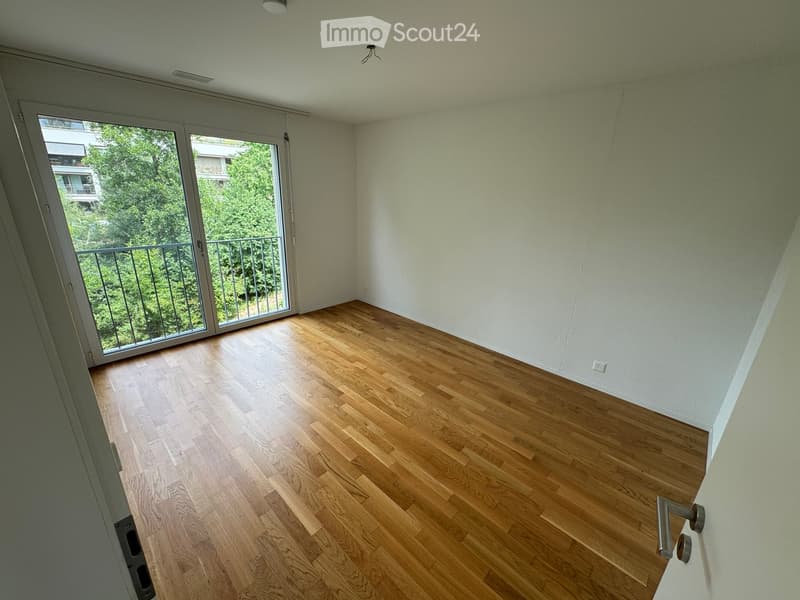 Empty room with wooden flooring, white walls, and large sliding glass door leading to a balcony with a metal railing.