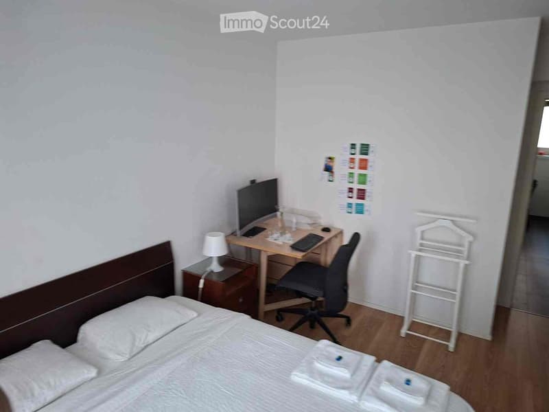 Cozy furnished room with a double bed, desk, chair, lamp, nightstand, and neatly arranged towels.