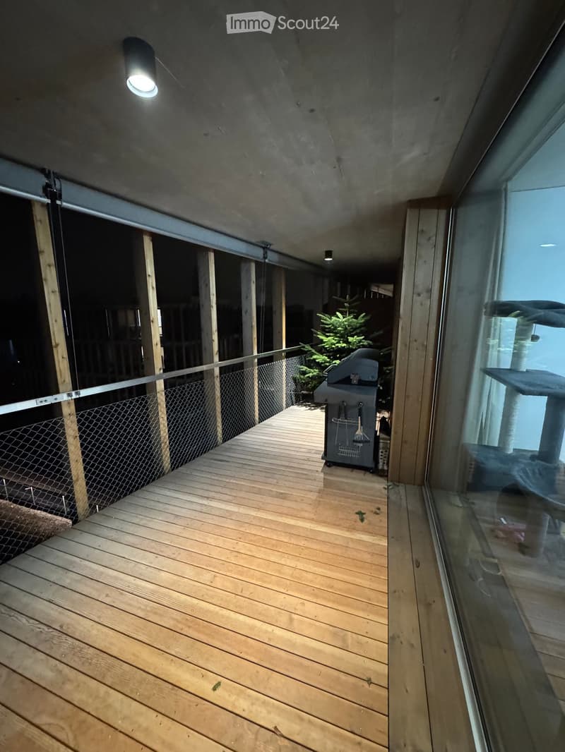 Wooden deck with railing, grill, and cat tree visible through large glass windows.