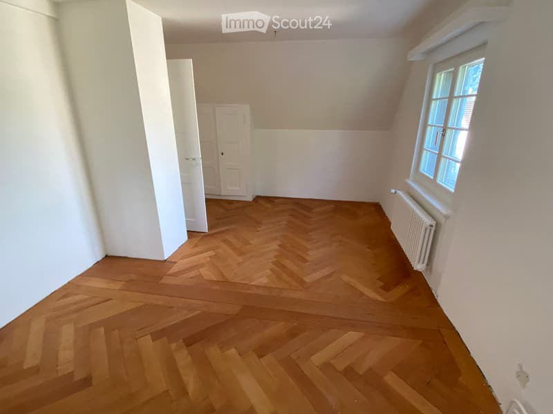 Empty room with wooden herringbone flooring, white walls, and a window with white frame. No furniture or equipment present.