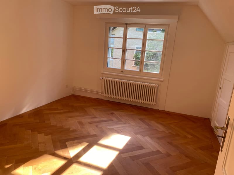 Empty room with wooden flooring, large windows, radiator, and a door.