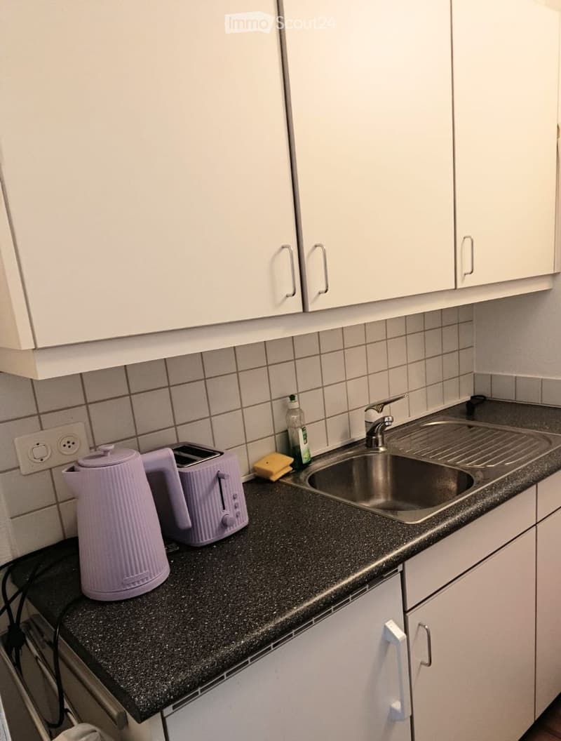 Modern kitchen with white cabinets, black granite countertop, stainless steel sink, electric kettle, toaster, and cleaning supplies.