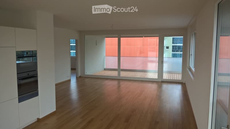 Empty room with wooden flooring, large sliding glass doors leading to a balcony, and a built-in oven unit on the left side.