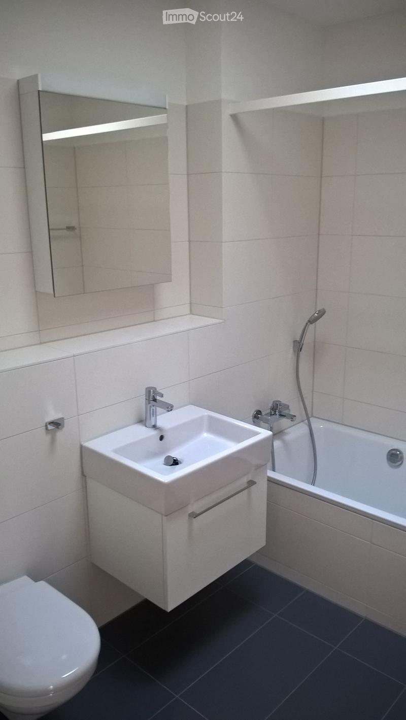Modern bathroom with white tiles, a white sink with a chrome faucet, a bathtub with a handheld shower, a toilet, and a wall-mounted mirror.