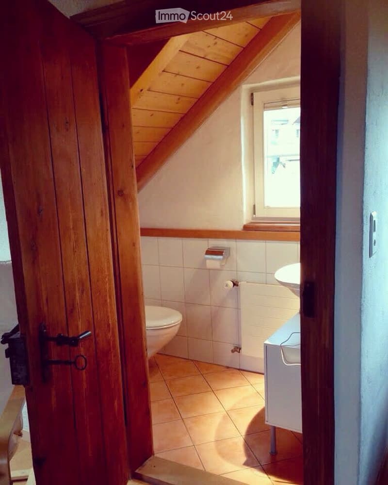 Cozy attic bathroom with wooden slanted ceiling, tiled floor, toilet, sink, and radiator.
