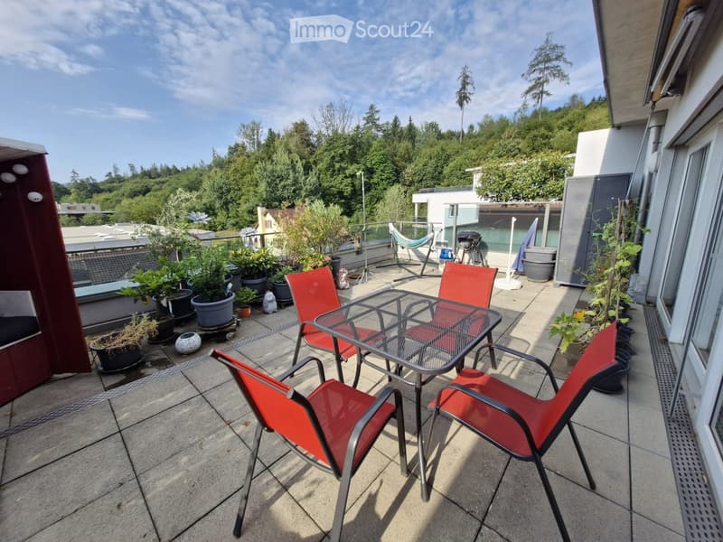 Balcony with a glass table, red chairs, potted plants, and a view of greenery.