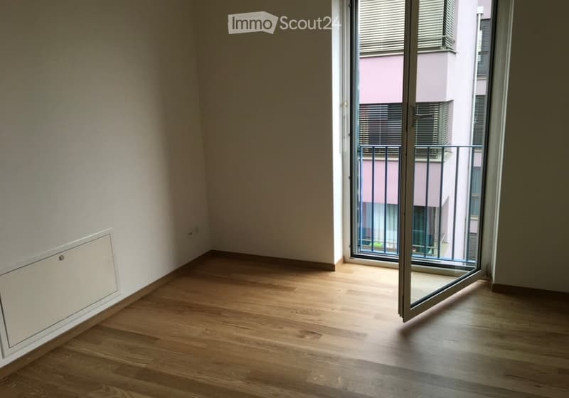 Empty room with wooden flooring, white walls, and a large sliding glass door leading to a balcony.